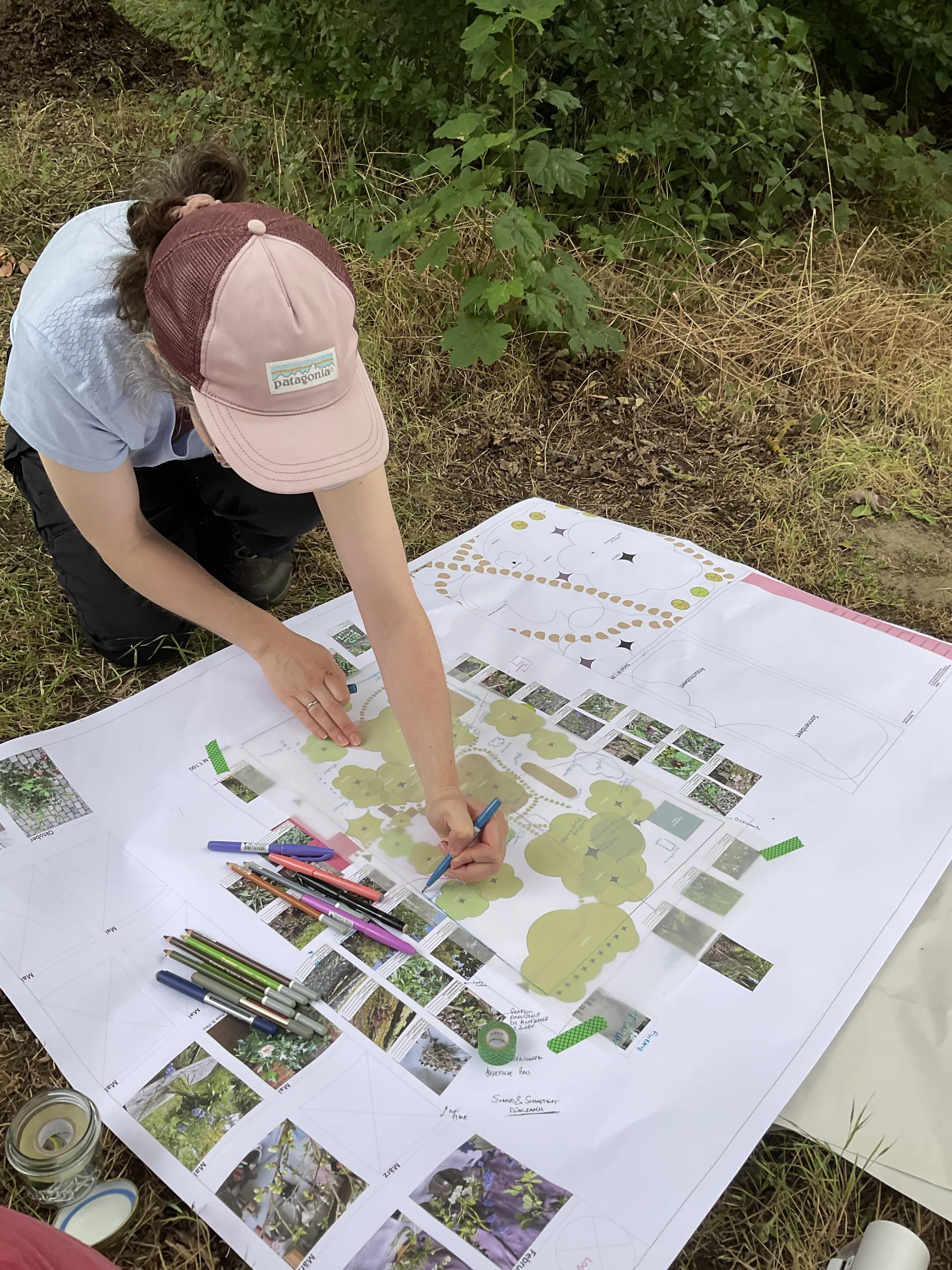 Frau mit Kappe legt Pflanzenkarten auf einen großen Gartenplan auf der Wiese