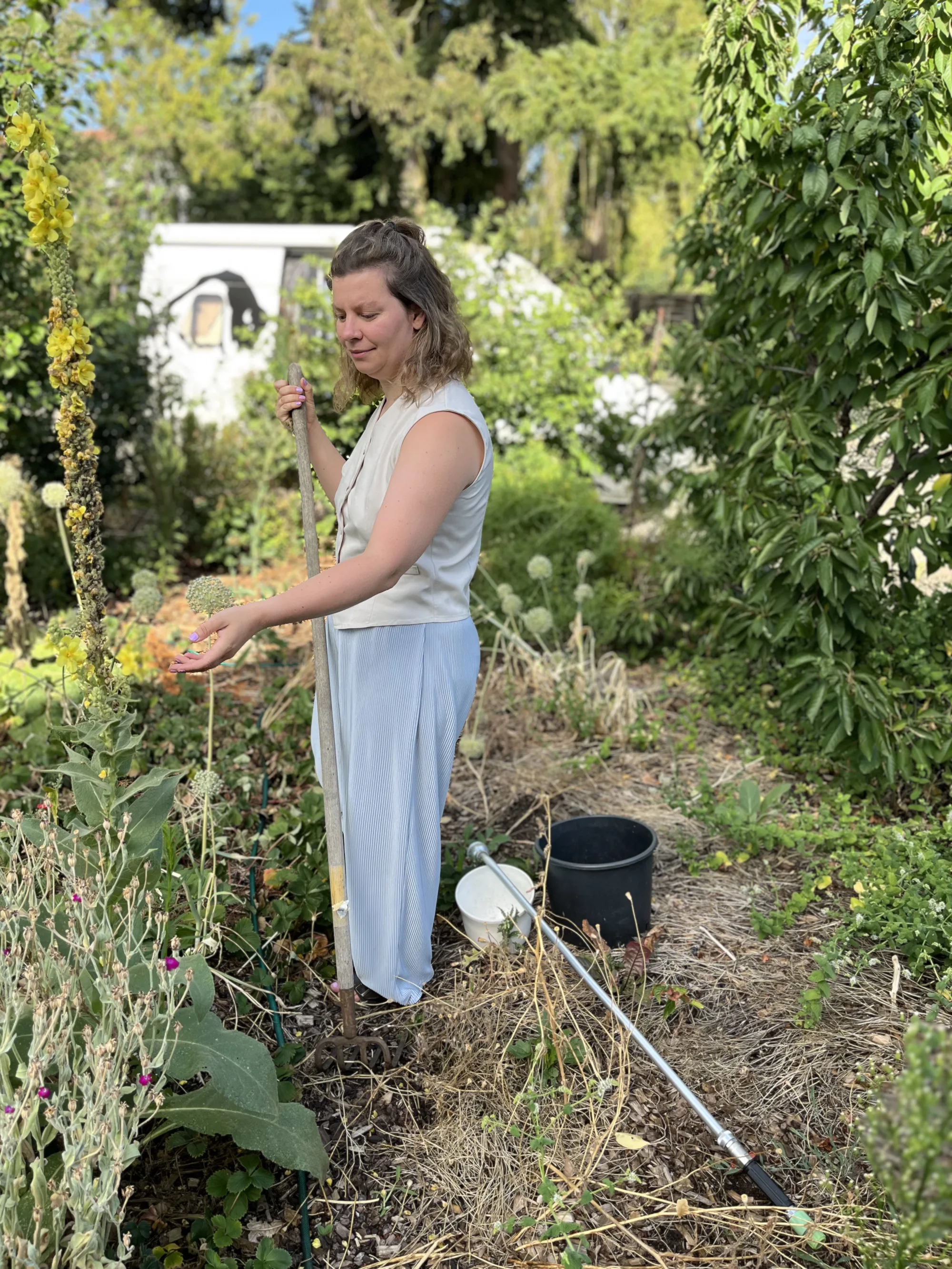 Frau steht zwischen hohen Pflanzen in einem naturnahen Garten und riecht an einer Blüte