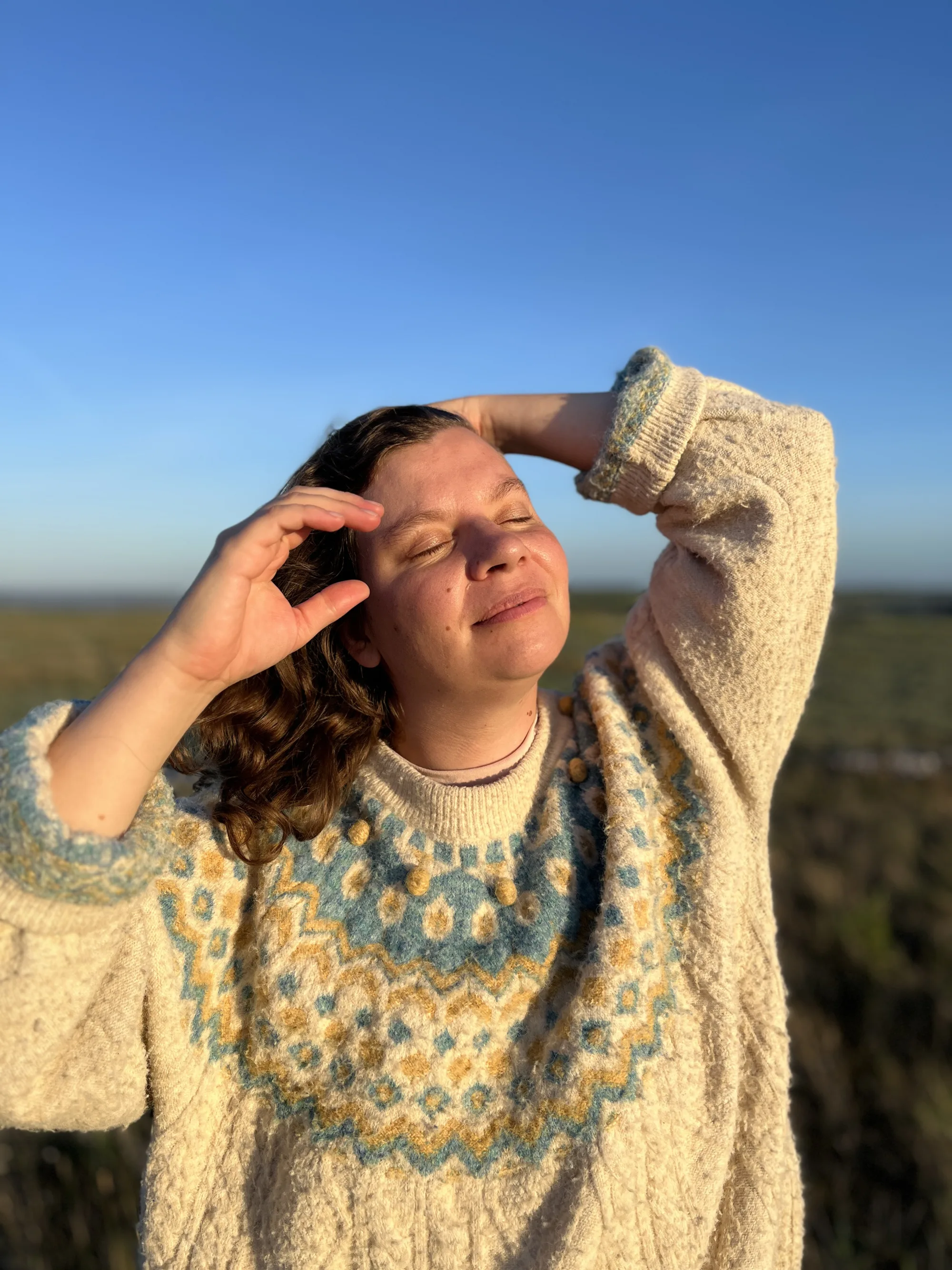 Maureen im Norwegerpulli hält sich die Hand gegen die Sonne über die Augen, dahinter blauer Himmel