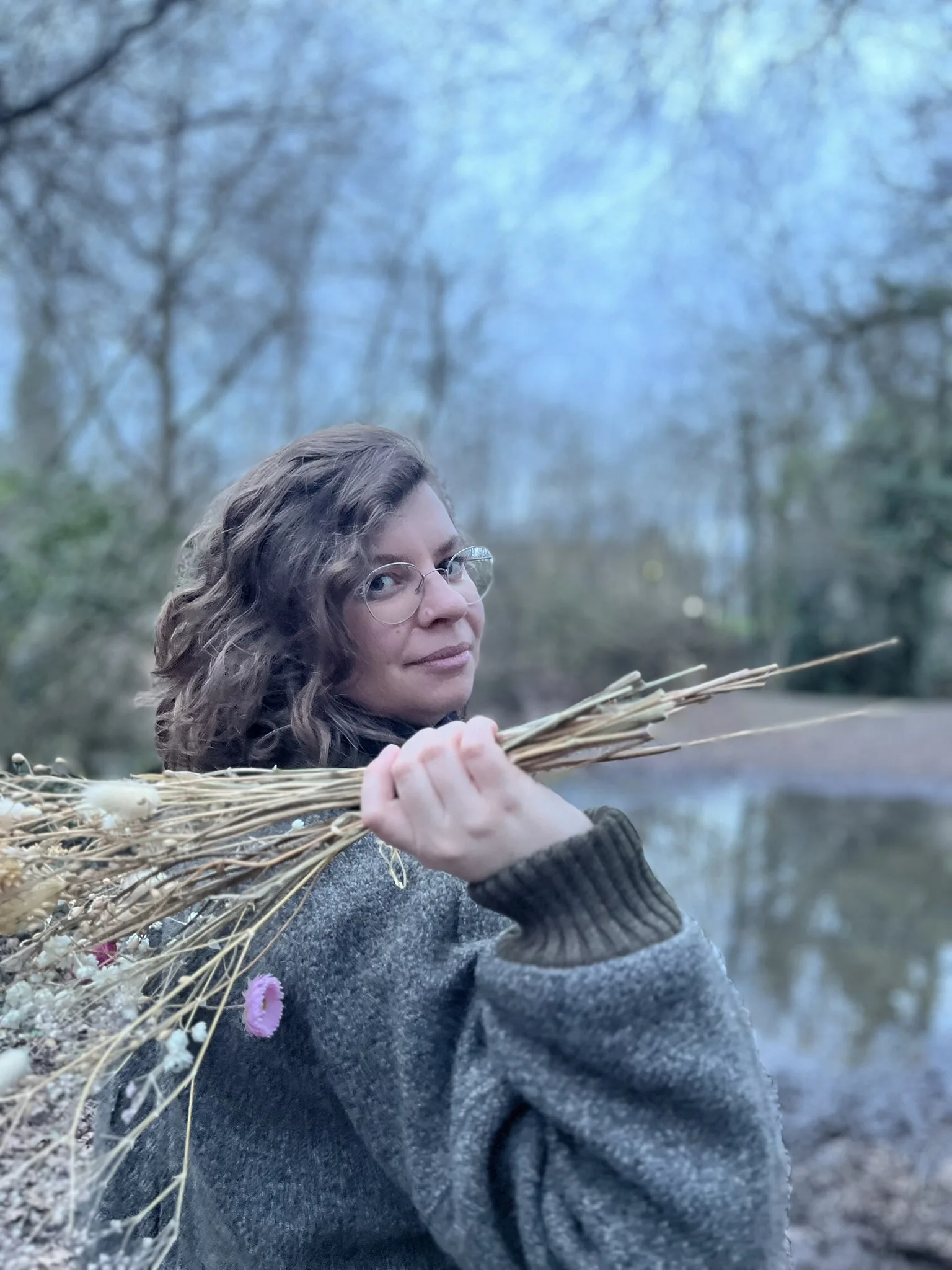 Maureen hält ein Bündel getrockneter Gräser an einem Teich im Wald