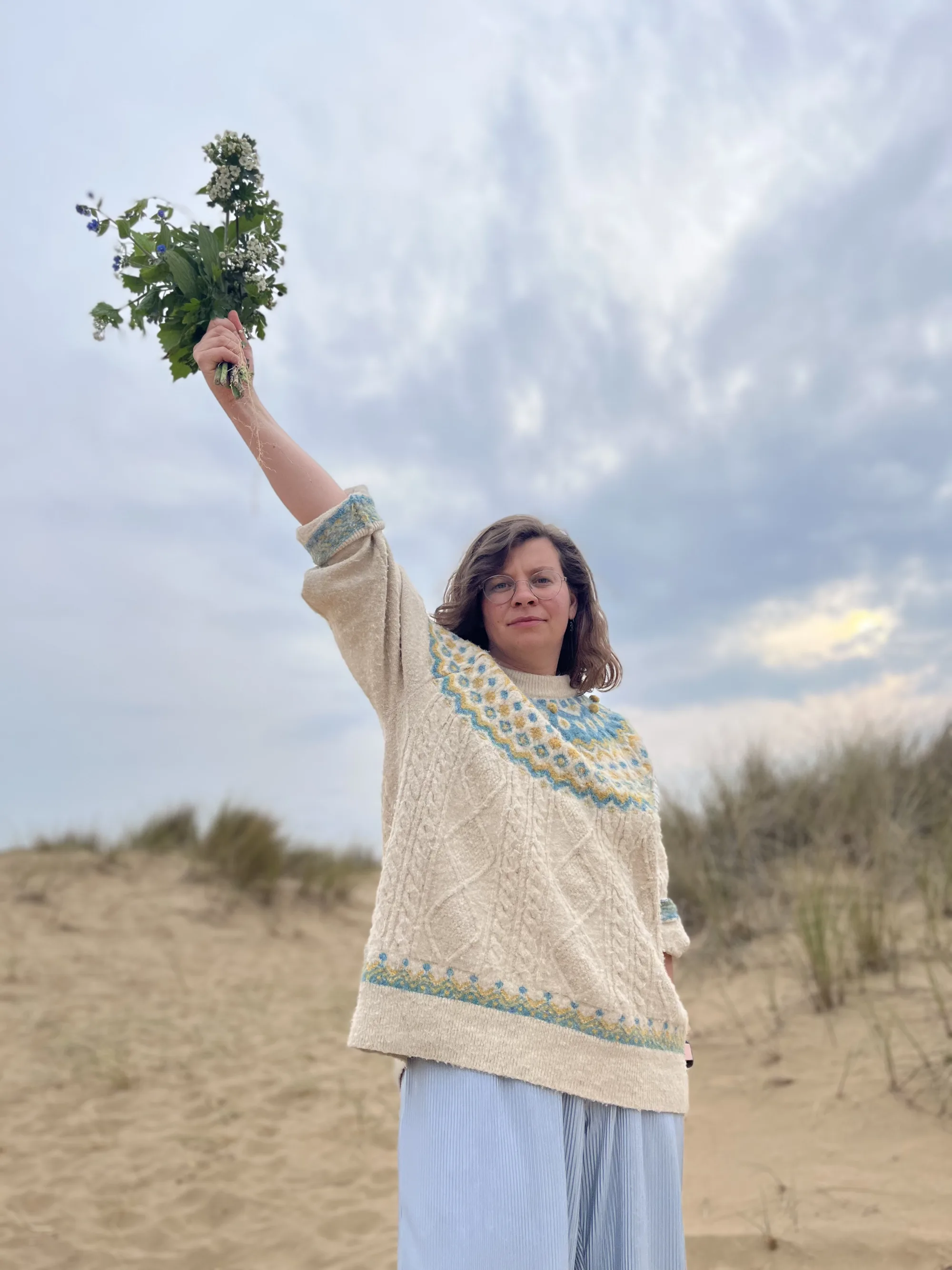 Maureen steht in den Dünen und hält einen Wildkräuterstrauß in den Himmel