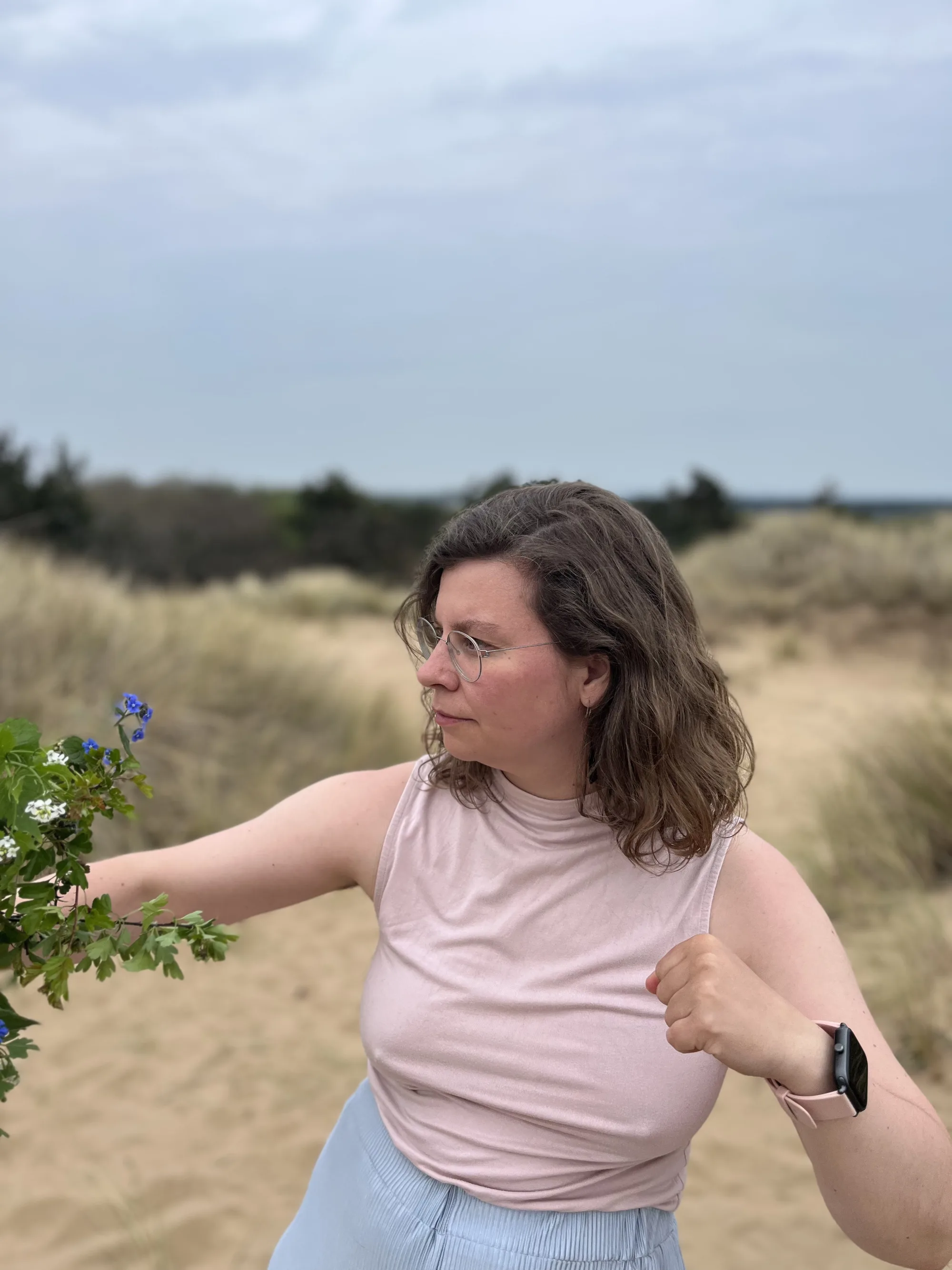 Maureen streckt in den Dünen einen blühenden Zweig zur Seite und schaut ihm nach