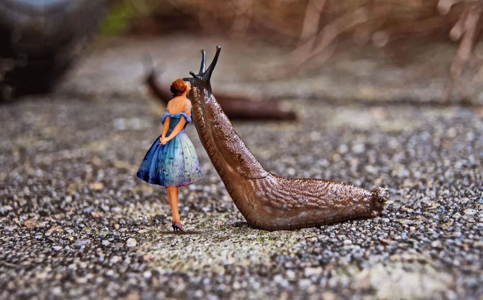 Nacktschnecke auf Kies, daneben eine kleine Figur einer Frau im blauen Kleid