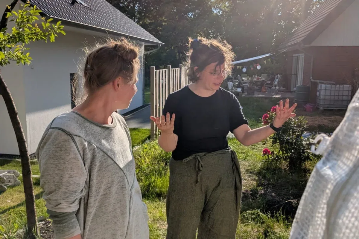 Zwei Frauen im Gespräch in einem Garten, eine erklärt etwas mit den Händen